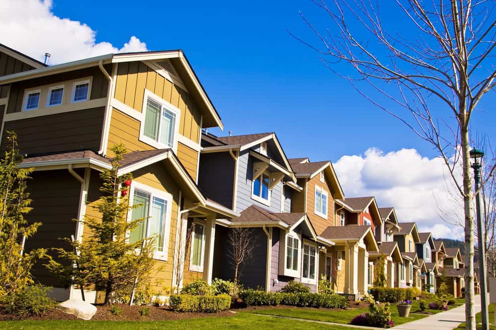 A row of colorful suburban houses with well-kept lawns, managed seamlessly by HOAs, sits under a clear blue sky.