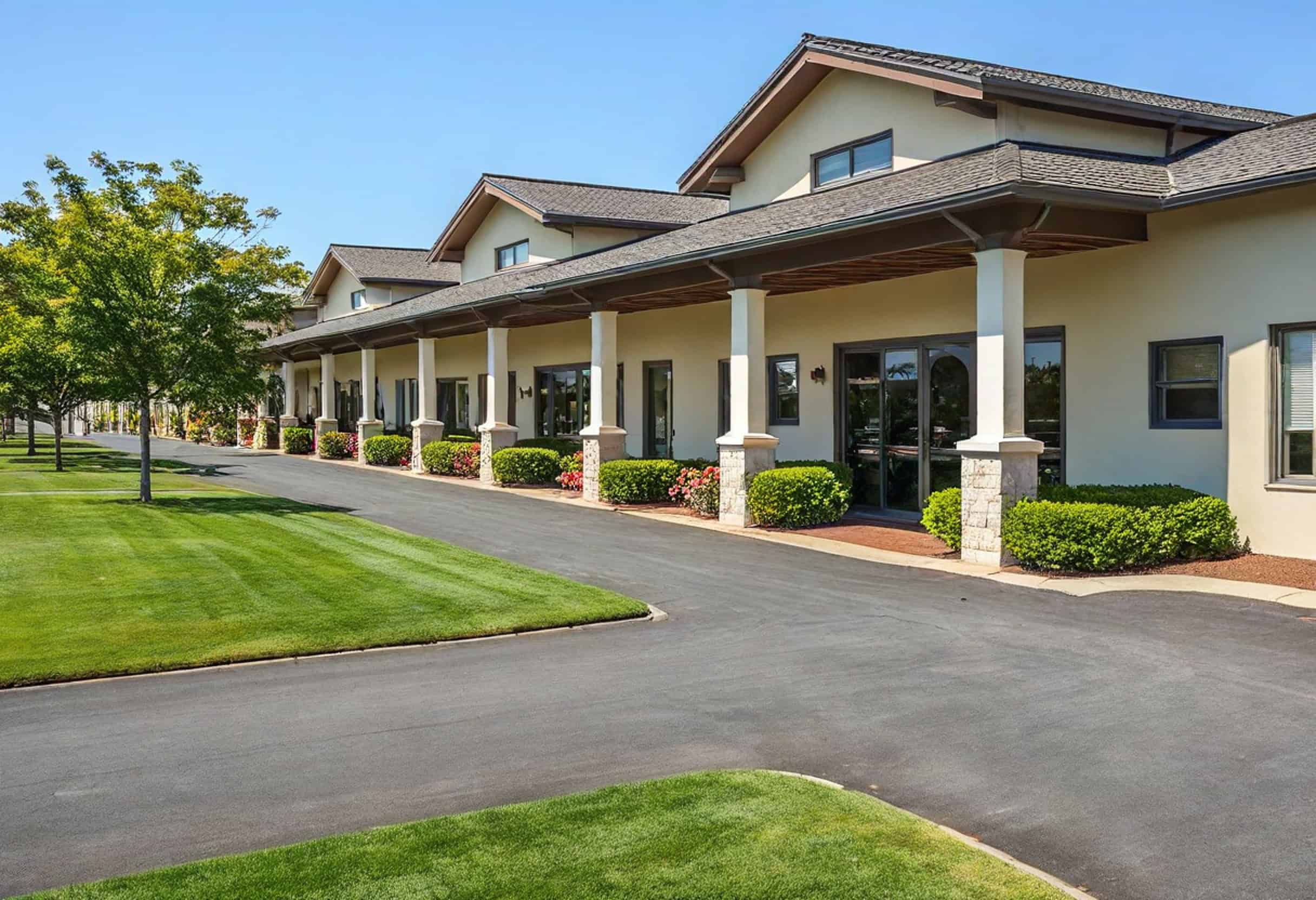 A long building with multiple arches, enveloped by meticulously maintained green lawns and trees, stands gracefully under a clear blue sky—a perfect example of exquisite retail landscaping.